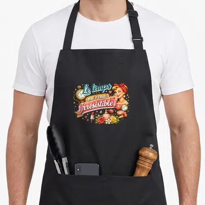 Tablier de cuisine noir avec illustration vintage femme blonde, rouge à lèvres, parfum et horloge dorée sur fond uni.