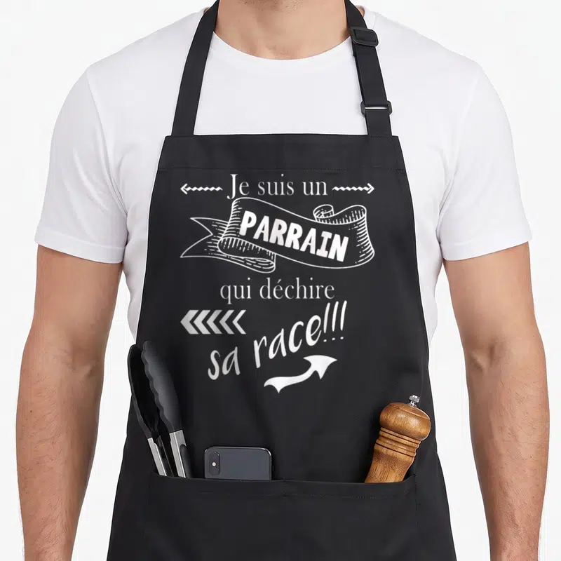 Tablier de cuisine noir avec inscription Je suis un parrain qui déchire sa race en typographie blanche vintage.