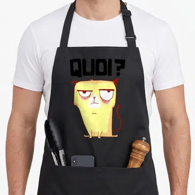 Tablier de cuisine noir avec un chat jaune aux yeux cernés et le texte quoi au-dessus.