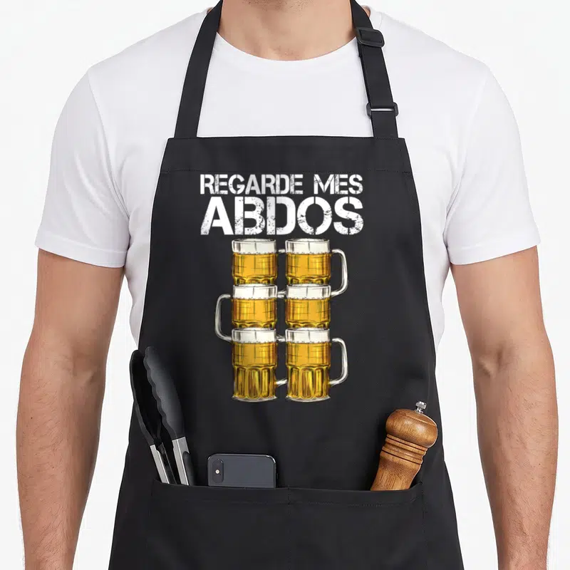 Tablier de cuisine noir avec six verres de bière empilés et le texte regarde mes abdos en blanc.