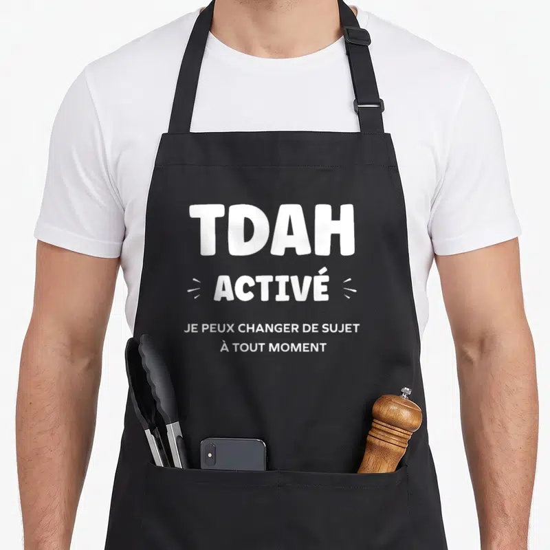 Tablier de cuisine noir avec l'inscription blanche TDAH ACTIVÉ et une phrase explicative humoristique centrée sur le motif.