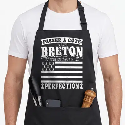 Tablier de cuisine noir avec inscription blanche humoristique sur fond de drapeau stylisé.