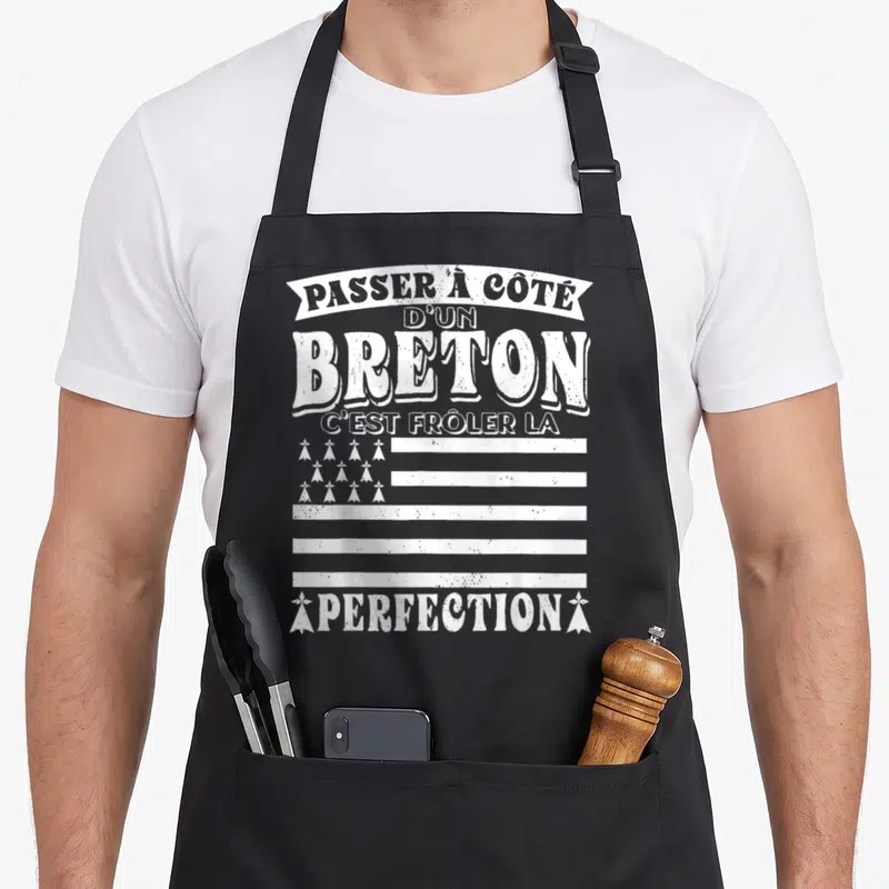 Tablier de cuisine noir avec inscription blanche humoristique sur fond de drapeau stylisé.