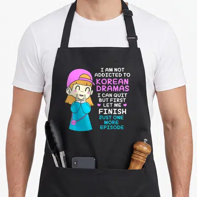 Tablier de cuisine noir avec illustration d'une fille en bonnet rose et texte sur les dramas coréens.