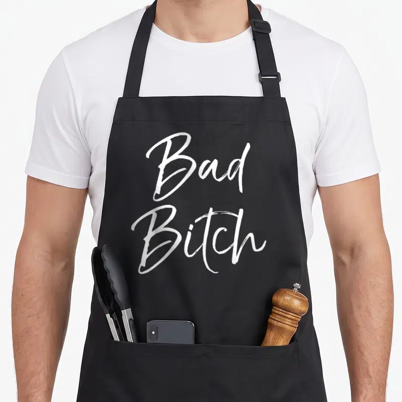 Tablier de cuisine noir avec l'inscription bad bitch en lettres blanches style calligraphie manuscrite.