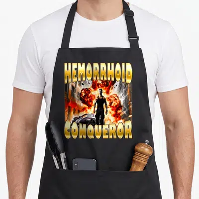 Tablier de cuisine noir avec homme musclé, explosion orange et texte doré HEMORRHOID CONQUEROR en lettres capitales.