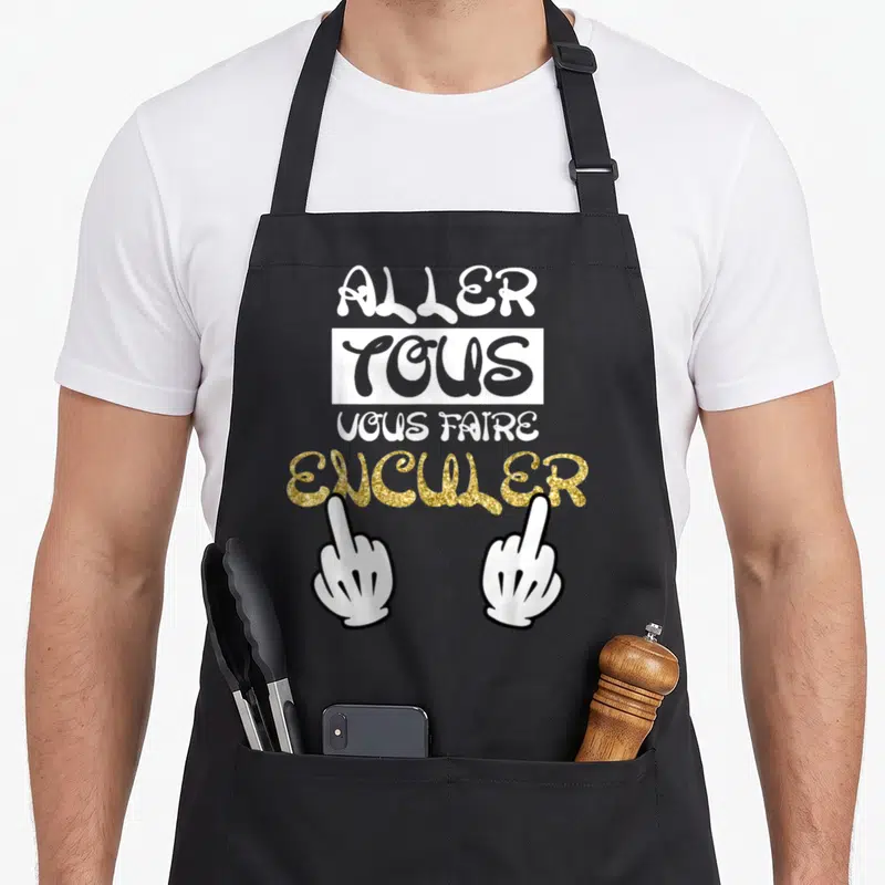 Tablier de cuisine noir avec inscription Aller tous vous faire enculer et deux doigts d'honneur gantés blancs sur fond gris.