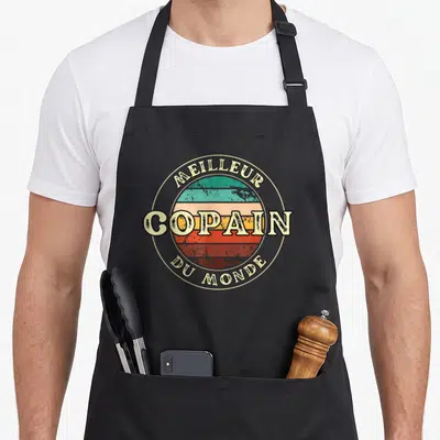 Tablier de cuisine noir avec logo circulaire retro affichant Meilleur Copain Du Monde sur fond de bandes colorées délavées.