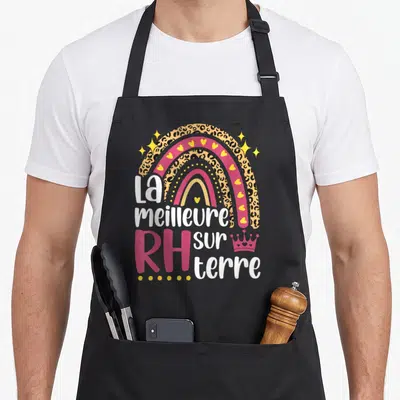 Tablier de cuisine noir avec arc-en-ciel léopard, cœurs jaunes et texte La meilleure RH sur terre en blanc et rose.