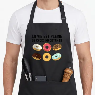 Tablier de cuisine noir avec six donuts colorés et le texte La vie est pleine de choix importants imprimé en noir.