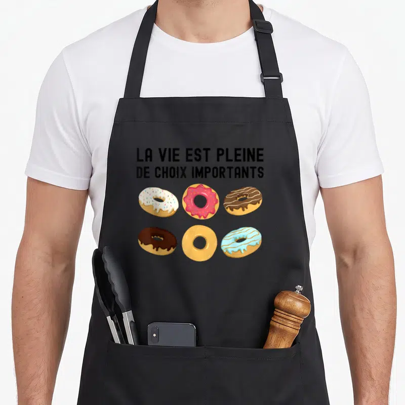 Tablier de cuisine noir avec six donuts colorés et le texte La vie est pleine de choix importants imprimé en noir.