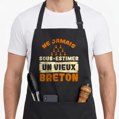 Tablier de cuisine noir avec linscription Ne jamais sous-estimer un vieux Breton en orange et gris.