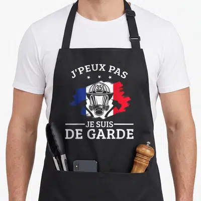 Tablier de cuisine noir avec illustration casque pompier 35 et texte J'peux pas je suis de garde sur fond tricolore.