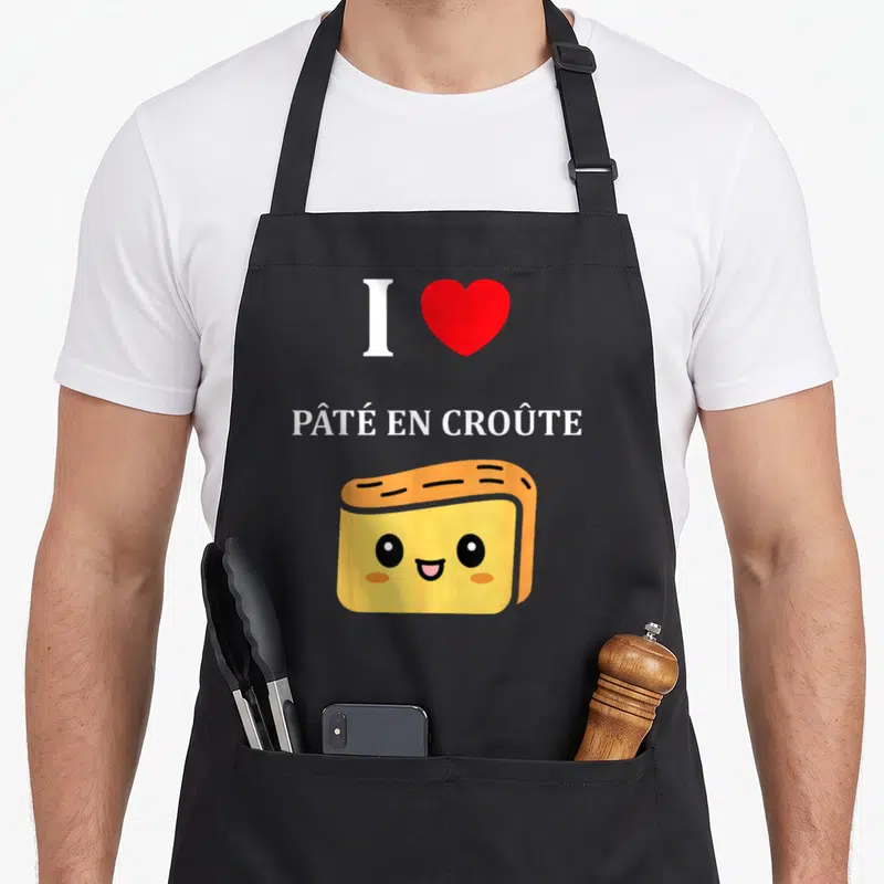 Tablier de cuisine noir avec un cœur rouge, le texte I love Pâté en croûte et une illustration souriante de pâté en croûte jaune et doré.