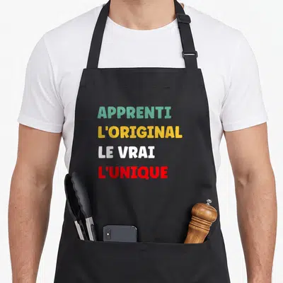 Tablier de cuisine noir avec inscription Apprenti L'Original Le Vrai L'Unique en lettres vertes jaunes blanches et rouges.