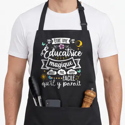 Tablier de cuisine noir avec inscription être une éducatrice magique n'est pas aussi facile qu'il y paraît entourée de papillons et d'une fleur.