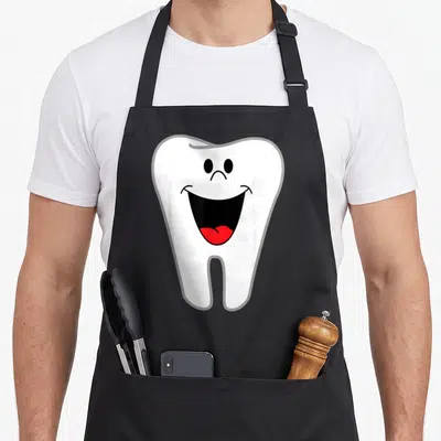Tablier de cuisine noir avec illustration d'une dent blanche au sourire rouge et joyeux en style cartoon simple.