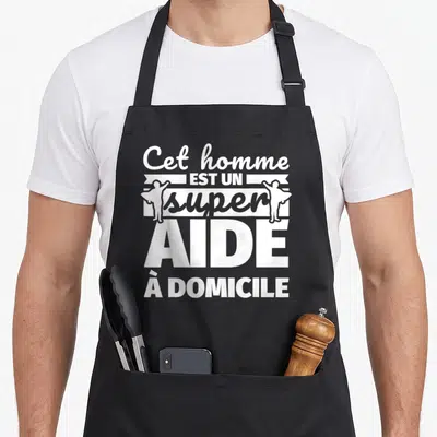 Tablier de cuisine noir avec inscription blanche Cet homme est un super aide à domicile et deux silhouettes d'hommes les bras écartés.