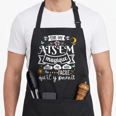 Tablier de cuisine noir avec inscription blanche Atsem magique et illustrations d'oiseaux, papillons et fleurs colorées.