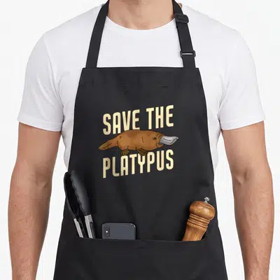 Tablier de cuisine noir avec illustration d'un ornithorynque et texte Save The Platypus en lettres capitales beige.