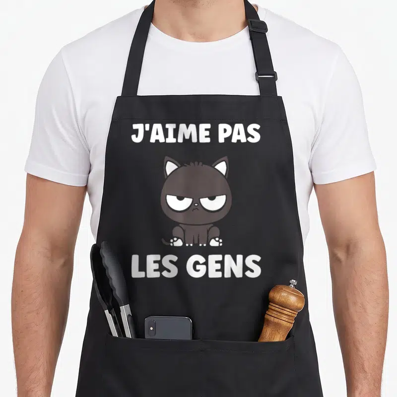 Tablier de cuisine noir avec un chat noir grognon et le texte blanc J'aime pas les gens imprimé au centre.