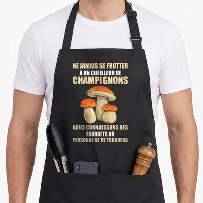 Tablier de cuisine noir avec illustration de trois cèpes et texte beige sur l'humour des cueilleurs de champignons sauvages.