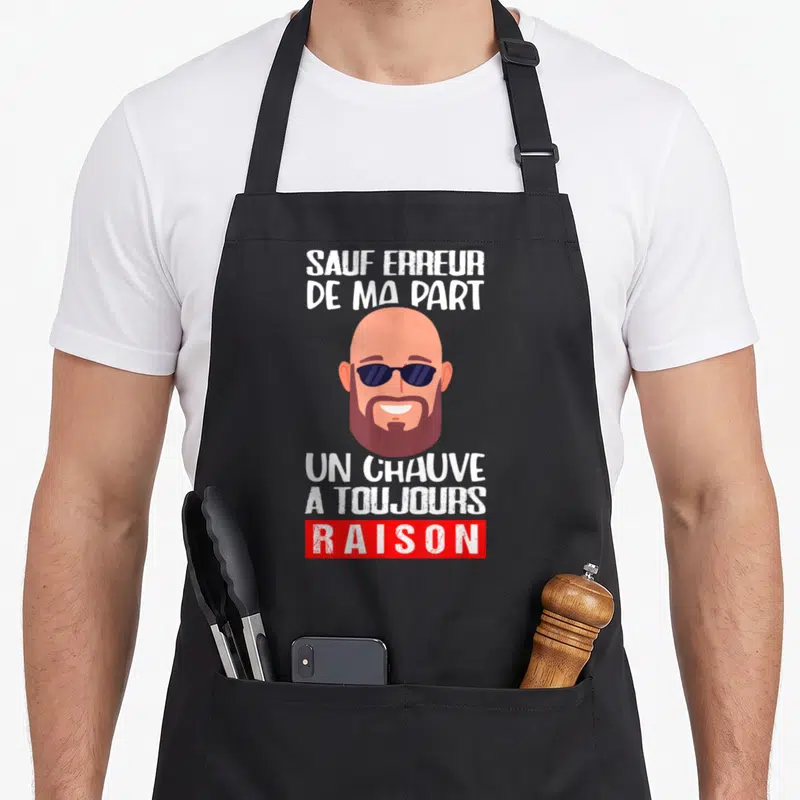 Tablier de cuisine noir avec illustration d'un homme chauve barbu portant des lunettes de soleil et du texte humoristique en blanc et rouge.