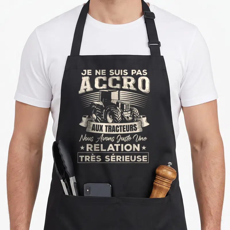 Tablier de cuisine noir avec illustration vintage d'un tracteur et texte humoristique en blanc.