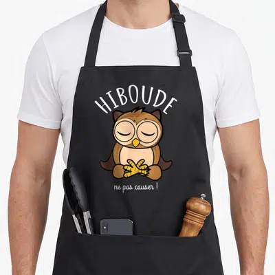 Tablier de cuisine noir avec un hibou marron aux yeux fermés et le texte Hiboude ne pas causer