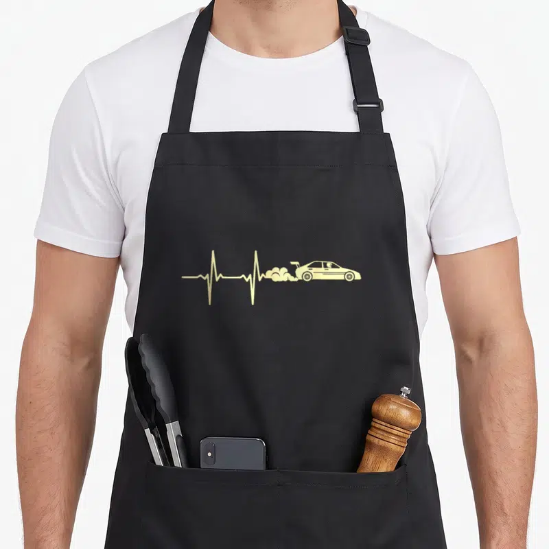 Tablier de cuisine noir avec un battement de cœur jaune se terminant par une silhouette de voiture de rallye fumante.