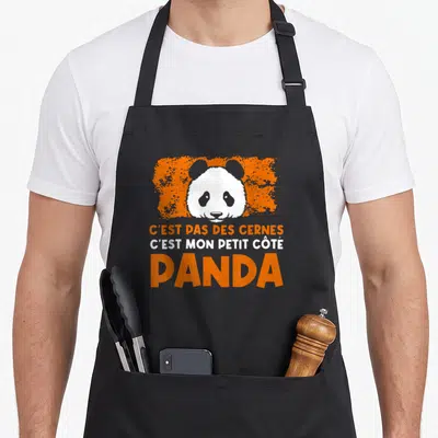 Tablier de cuisine noir avec tête de panda et texte Cest pas des cernes cest mon petit côté panda en orange et blanc.