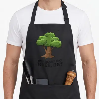 Tablier de cuisine noir avec illustration d'un arbre vert et texte anglais humoristique sous le dessin.