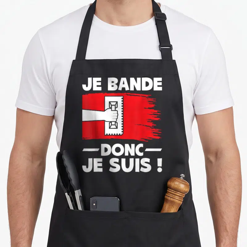 Tablier de cuisine noir avec une illustration de main tenant un outil de jointage blanc sur une bande rouge et du texte en majuscules.