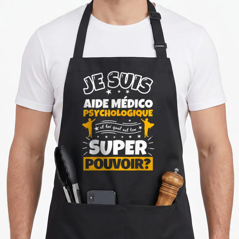 Tablier de cuisine noir avec inscription Je suis aide médico psychologique et toi quel est ton super pouvoir en blanc et orange.