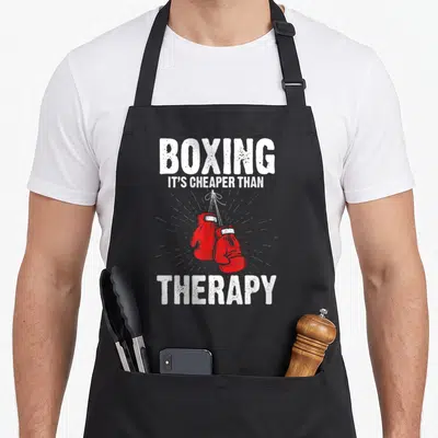 Tablier de cuisine noir avec gants de boxe rouges suspendus et texte blanc humoristique sur fond uni.