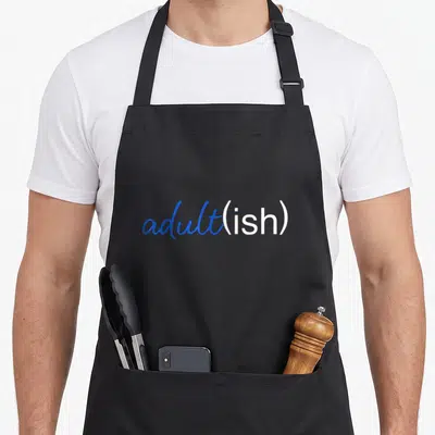 Tablier de cuisine noir avec l'inscription adult(ish) en bleu et blanc sur le devant.