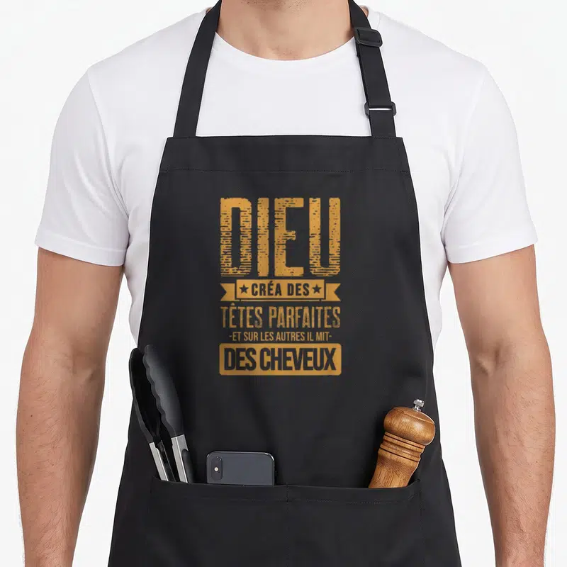 Tablier de cuisine noir avec une inscription dorée humoristique sur la calvitie et les cheveux.
