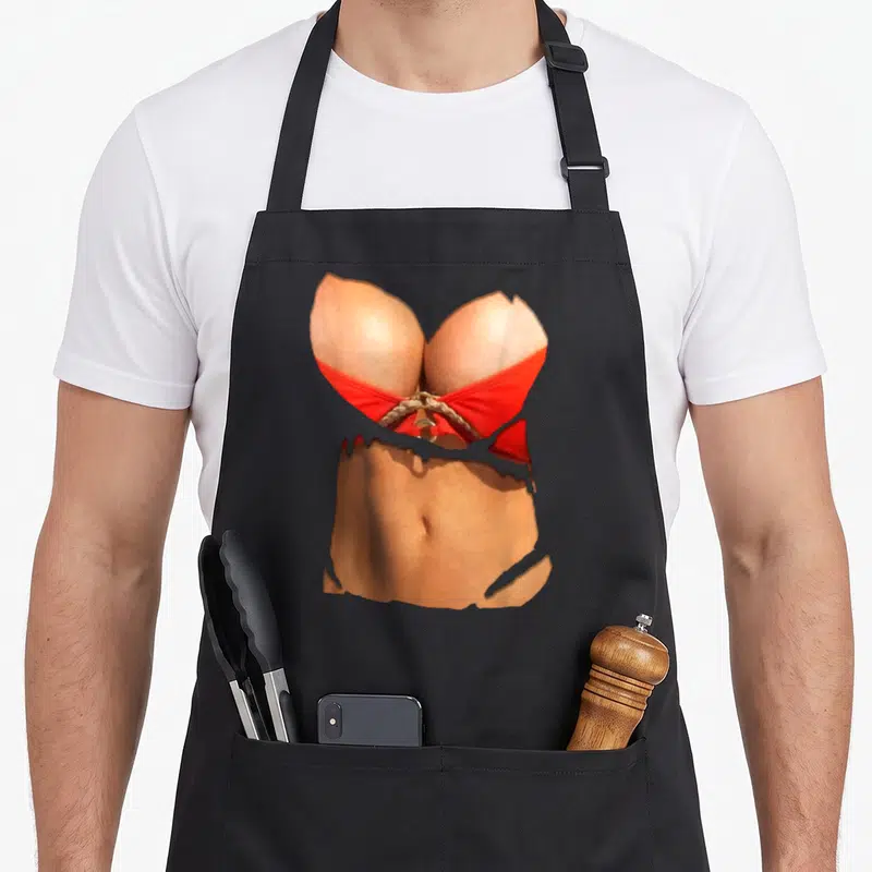 Tablier de cuisine noir avec motif imprimé représentant un haut de bikini rouge et un ventre sculpté sur fond gris uni.