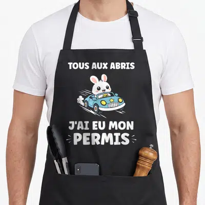 Tablier de cuisine noir avec un lapin blanc au volant d'une voiture bleue et le texte Tous aux abris J'ai eu mon permis