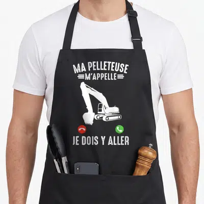Tablier de cuisine noir avec silhouette blanche de pelleteuse et texte humoristique sur fond gris uni.