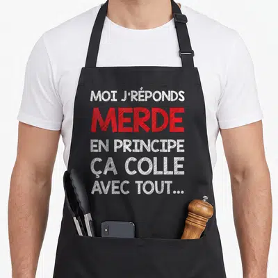 Tablier de cuisine noir avec inscription typographique blanche et rouge sur fond uni.