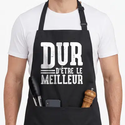 Tablier de cuisine noir avec l'inscription blanche dur d'être le meilleur en typographie épaisse et texturée.