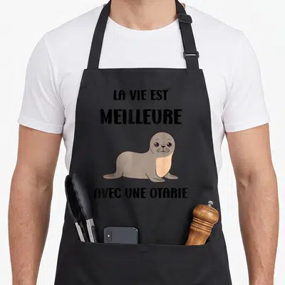 Tablier de cuisine noir avec illustration d'une otarie grise et texte noir La vie est meilleure avec une otarie.