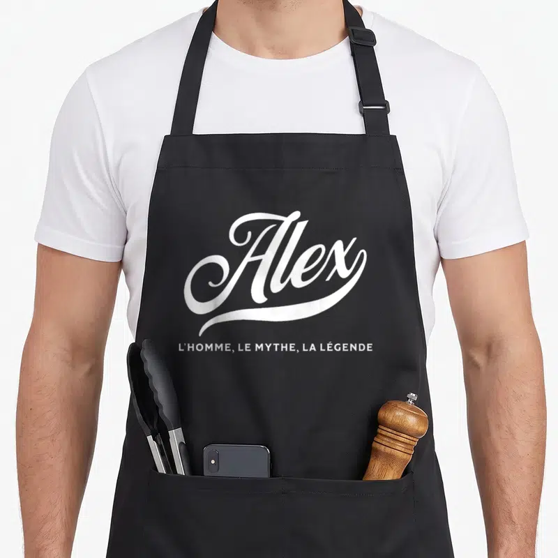 Tablier de cuisine noir avec le nom Alex en calligraphie blanche et la mention l'homme le mythe la légende en dessous.