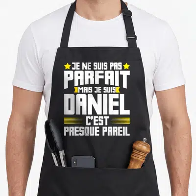 Tablier de cuisine noir avec l'inscription blanche et jaune Je ne suis pas parfait mais je suis Daniel c'est presque pareil.