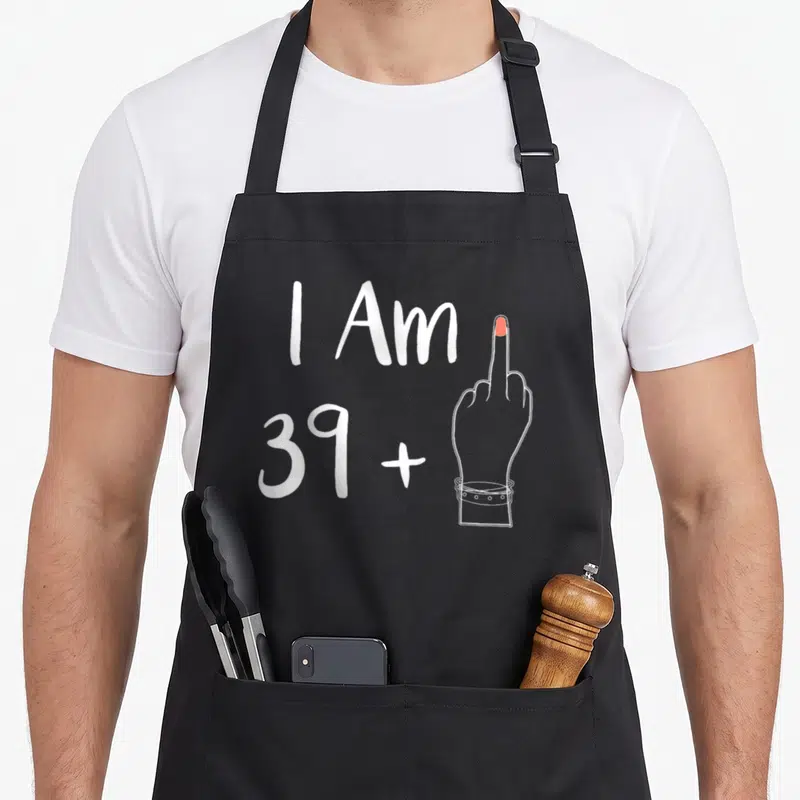 Tablier de cuisine noir avec l'inscription I Am 39+ et une main gantée levant le majeur en blanc.