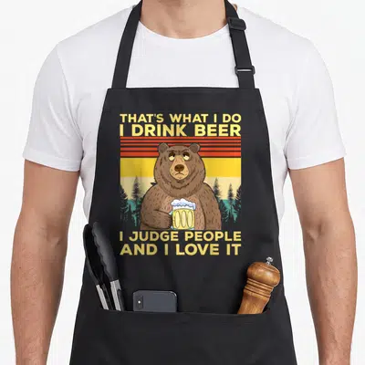 Tablier de cuisine noir avec un ours tenant une chope de bière et un regard sarcastique.