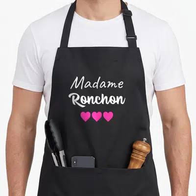Tablier de cuisine noir avec l'inscription Madame Ronchon en blanc et trois coeurs roses alignés en dessous.