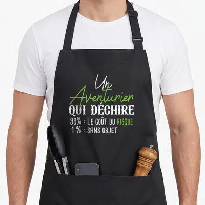 Tablier de cuisine noir avec l'inscription Un Aventurier qui déchire 99 pour cent le goût du risque en typographie blanche et verte.