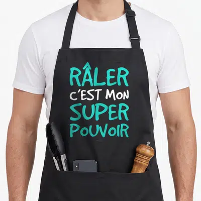 Tablier de cuisine noir avec l'inscription râler c'est mon super pouvoir en lettres turquoise et blanches.
